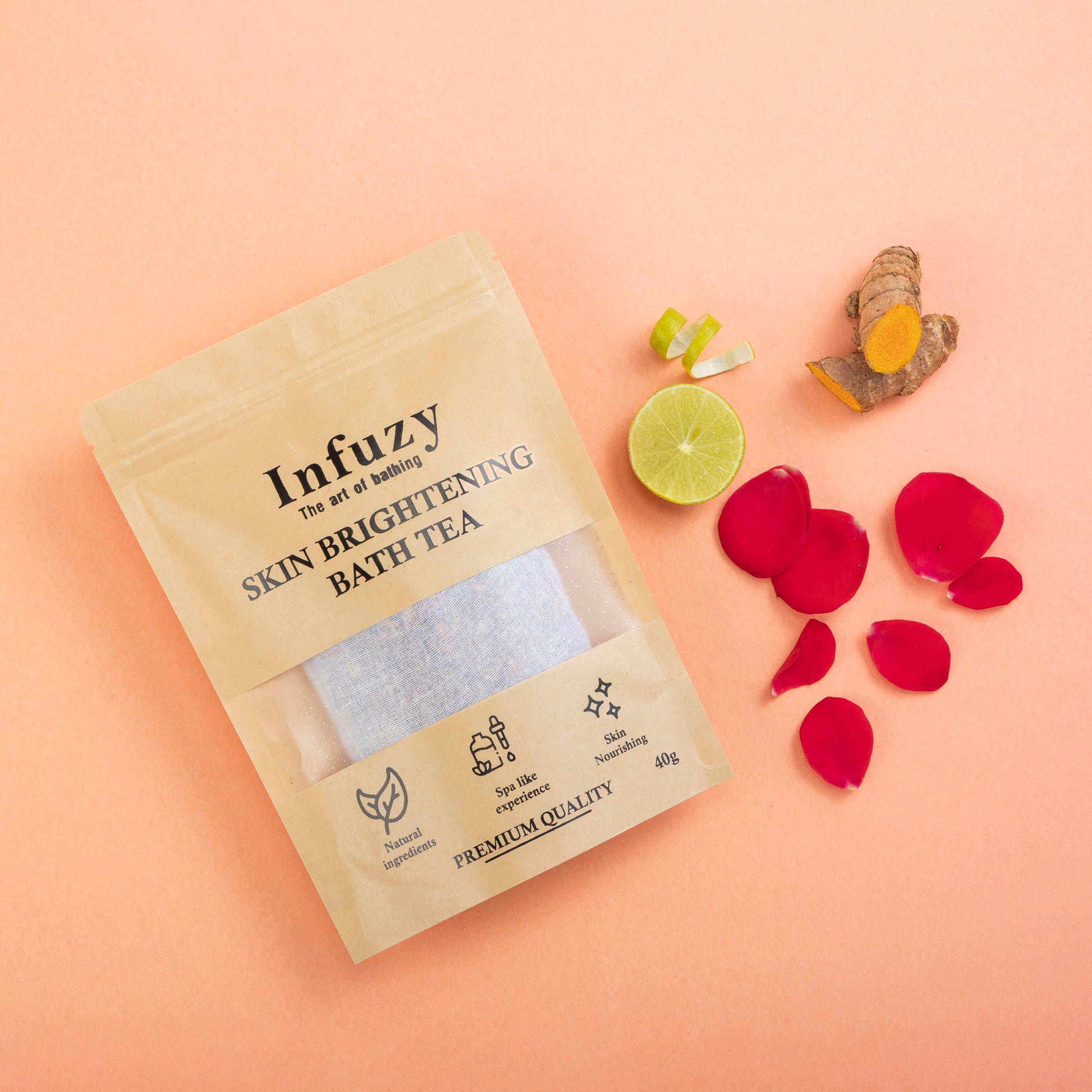 A packaged Skin Brightening Bath Tea bag from Infuzy with ingredients like turmeric, rose petals, and coconut milk powder displayed around it on a pink background.
