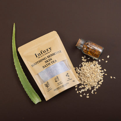 A package of 'Innuzy Soothing Sensitive Skin Bath Tea' with loose tea leaves, a slice of aloe vera, and oats spread out on a dark background.