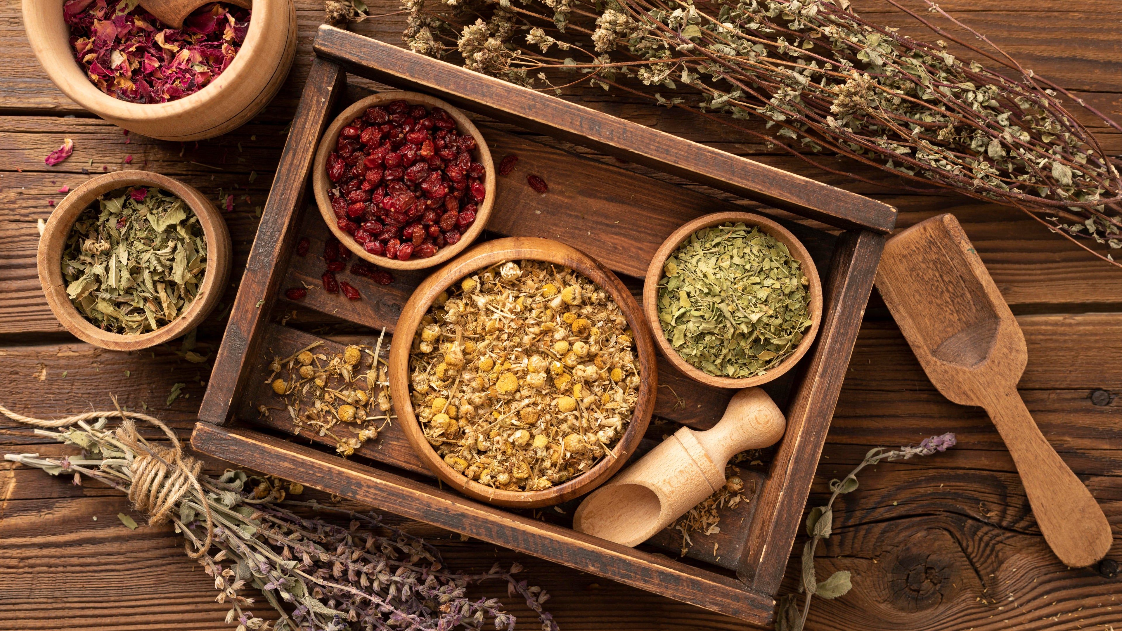 Wooden tray with various dried herbs on a wooden surface